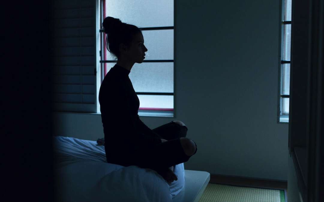 woman sitting on edge of bed thinking
